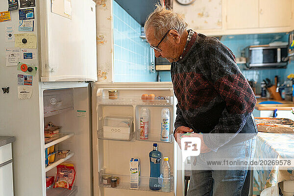 90-year-old senior in his kitchen looking for a dessert in his fridge.