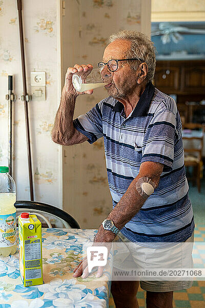 90 year old senior drinking lemonade and wearing a bandage on his left elbow.