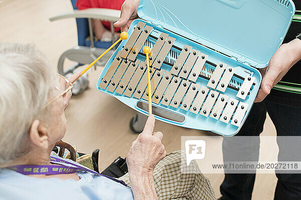 EHPAD - Elderly resident tapping on a xylophone during a musical activity.