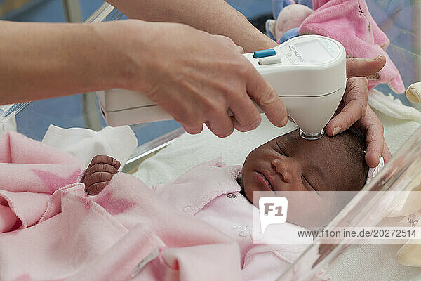 Midwife measuring the bilirubin level in a newborn using a bilirubinometer.