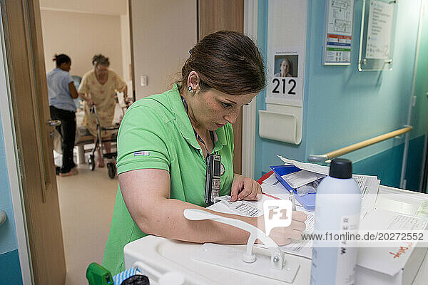 EHPAD - Nurse checking the drug prescriptions of a resident in front of her room while a caregiver takes care of her.