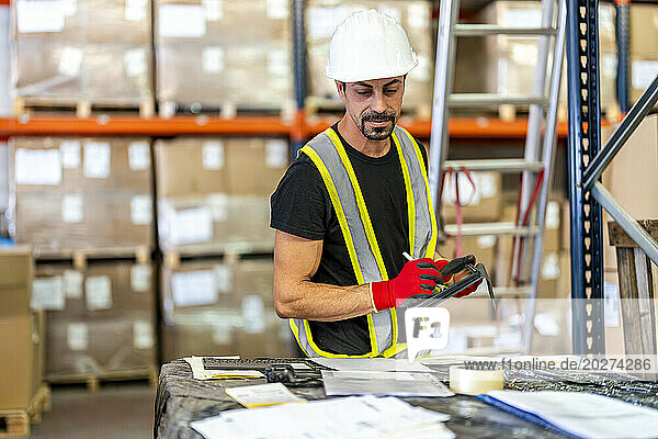 Worker examining documents with tablet PC at warehouse