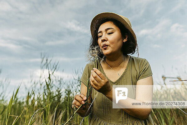 Carefree woman wishing with dandelion in field