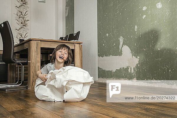 Playful boy wrapped in white wallpaper having fun at home