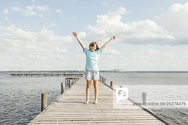 Happy girl standing on wooden pier at lake