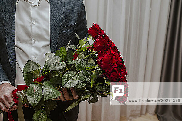 Boy wearing suit and holding bouquet of red roses at home