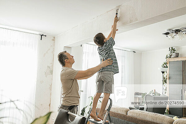 Son helping father in peeling old wallpaper from wall at home
