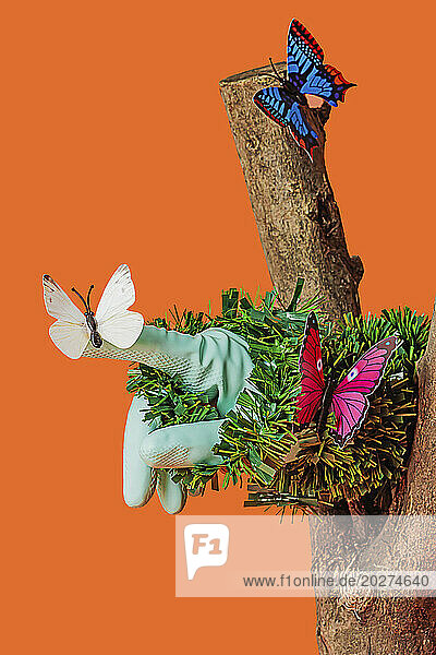 Artificial butterflies sitting on grass and tree trunk against orange background