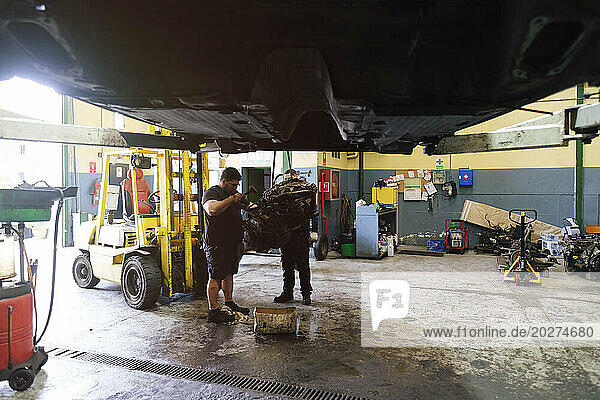 Auto mechanic colleagues working on machine part at workshop