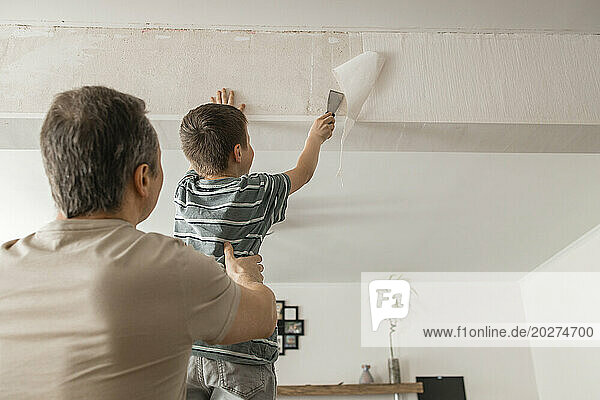Son and father peeling old wallpaper with spatula from wall at home