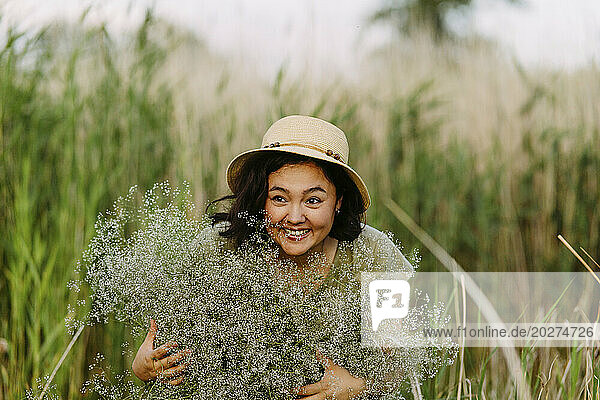 Cheerful woman holding bunch of gypsophila flowers in field