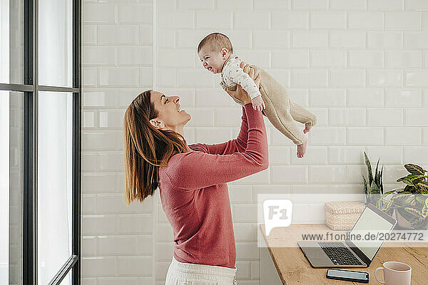 Happy freelancer mother playing with baby girl in kitchen at home