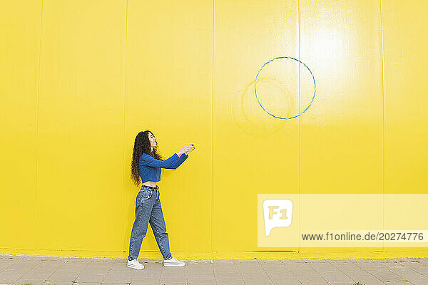 Woman throwing hula hoop standing against yellow background