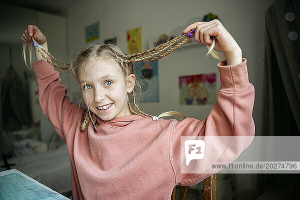 Playful girl holding pigtails sitting at home