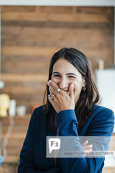 Happy businesswoman with hand covering mouth at home