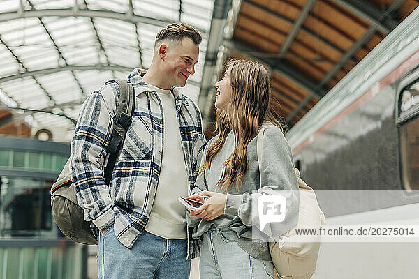 Young couple with backpacks standing at railroad station