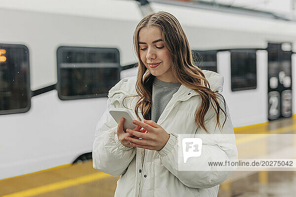Smiling woman using smart phone at railroad station