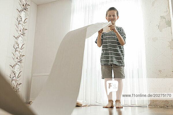 Happy boy playing with roll of wallpaper at home