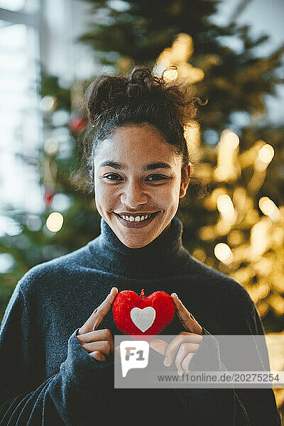 Smiling woman with red heart shape at home
