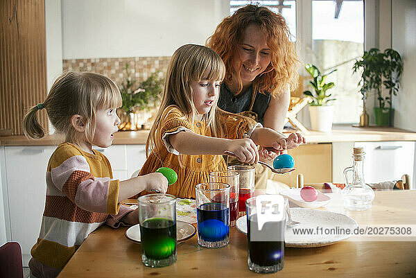 Mother and daughters dyeing Easter eggs at home