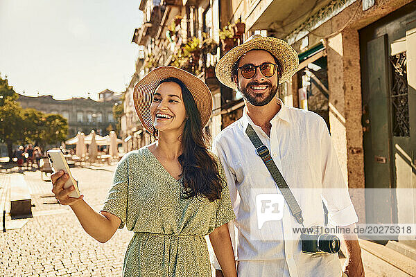 Happy woman holding smart phone with man on street near buildings
