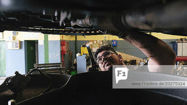 Mechanic using flashlight and inspecting lifted vehicle at workshop