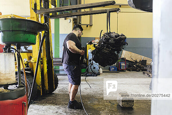 Mechanic examining engine hanging from forklift at workshop