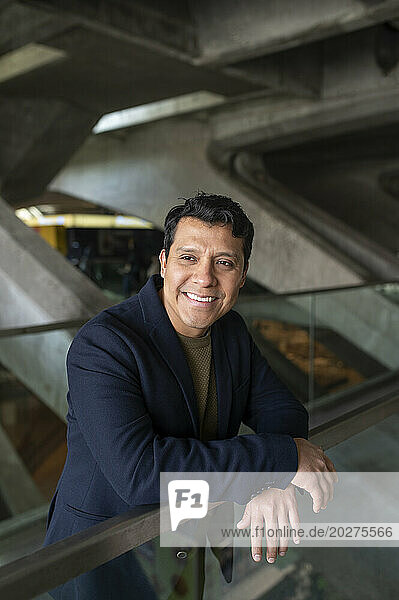 Happy businessman wearing blazer and leaning on railing