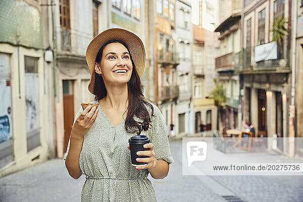 Smiling woman holding coffee cup and traditional dessert pastel de nata