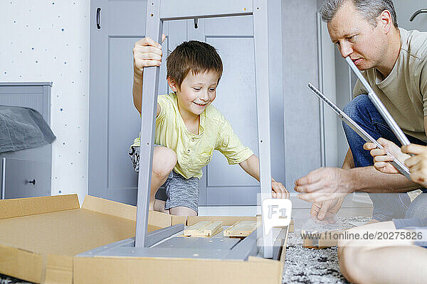 Smiling boy assembling nightstand with father at home