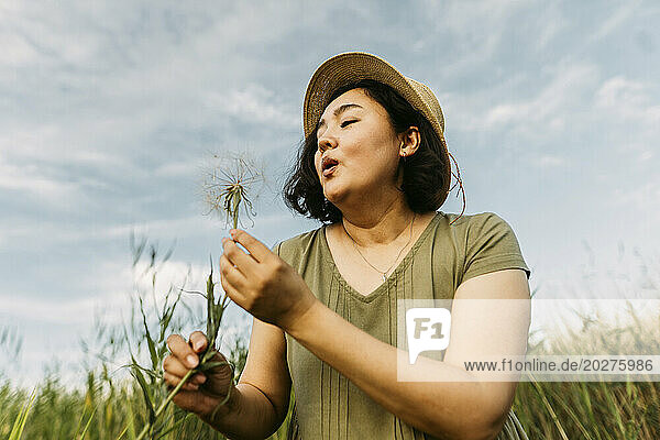 Playful woman blowing on dandelion in field