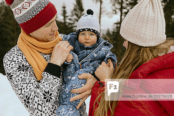 Cute baby boy with parents in winter forest