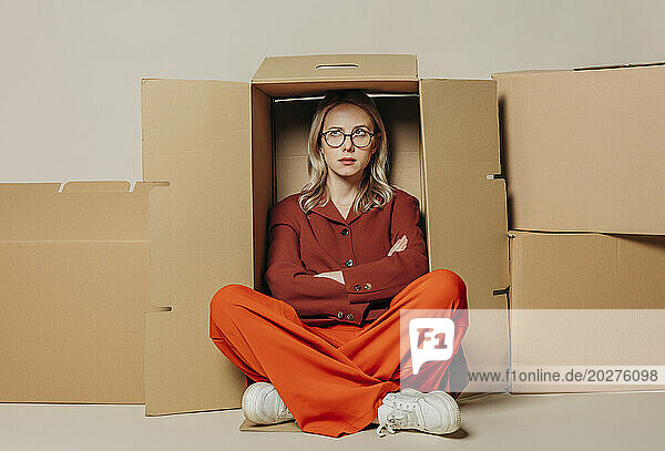 Upset businesswoman sitting with arms crossed in carton box against white background