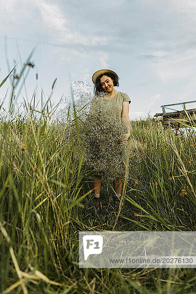 Smiling mature woman holding bunch of gypsophila flowers amidst grass in field
