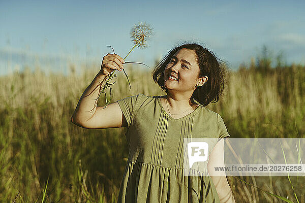 Smiling mature woman holding dandelion in field on sunny day