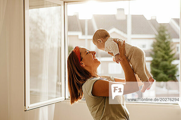 Happy woman playing with baby daughter near window