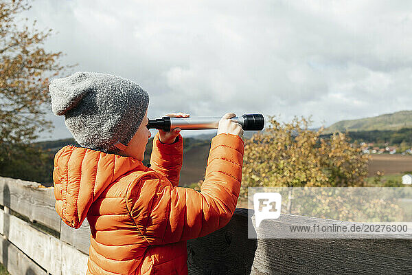 Boy wearing jacket and looking through telescope