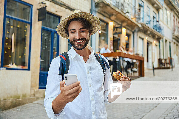 Happy young man holding traditional Portuguese dessert and using smart phone