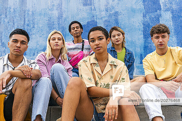 Confident young people sitting on steps in front of wall