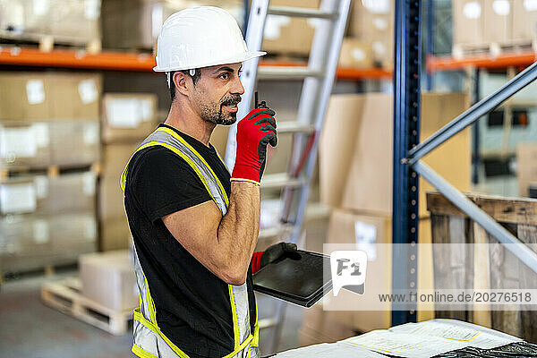 Worker talking on walkie-talkie and holding tablet PC at warehouse