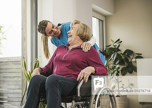 Happy home caregiver with senior woman sitting in wheelchair