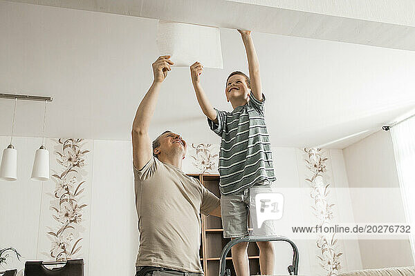 Happy boy and father peeling old wallpaper from ceiling at home