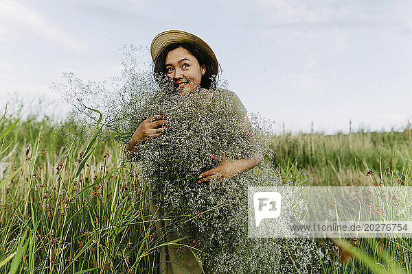 Happy mature woman embracing bunch of gypsophila flowers in field