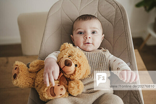 Cute baby girl sitting with stuffed toy on bouncer chair
