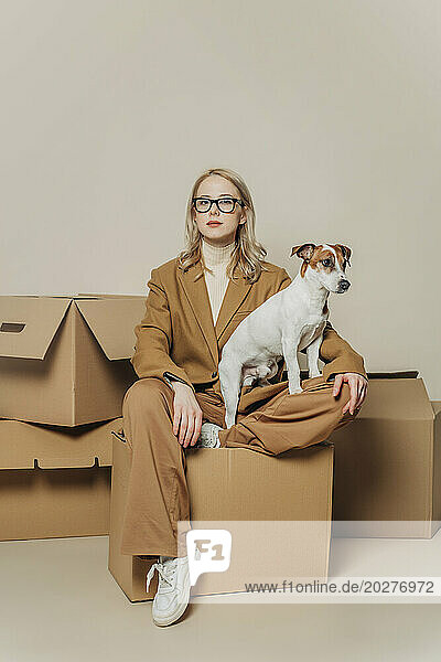 Businesswoman sitting with dog on carton box against white background