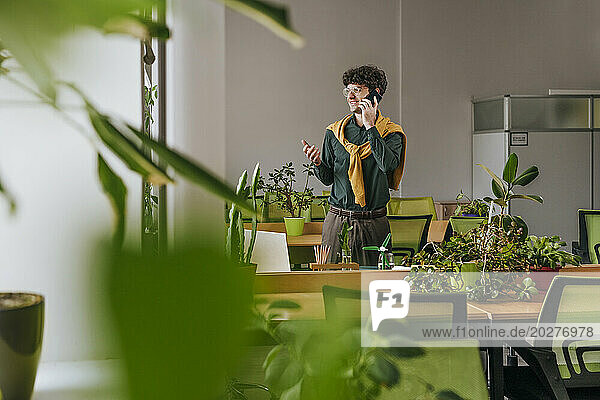 Businessman talking on smart phone near plants in office