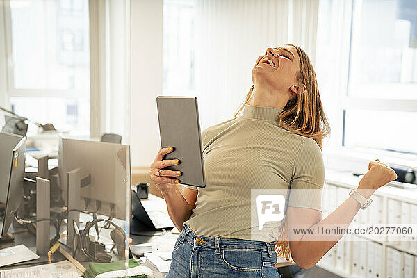 Excited businesswoman with tablet PC celebrating success in office