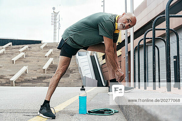 Retired senior man tying shoelace by parallel bars