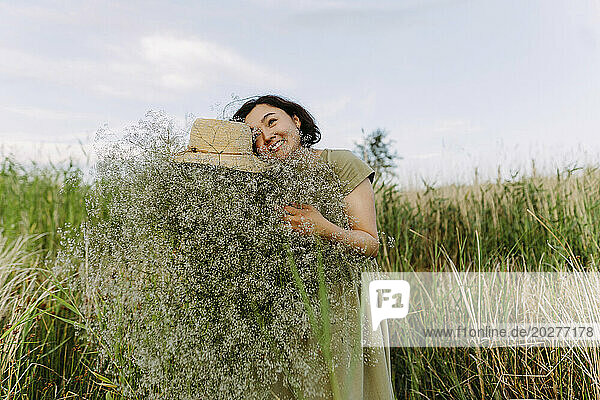 Carefree mature woman with bunch of gypsophila flowers in field