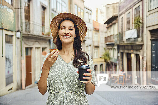 Smiling woman holding coffee cup and traditional dessert pastel de nata in city